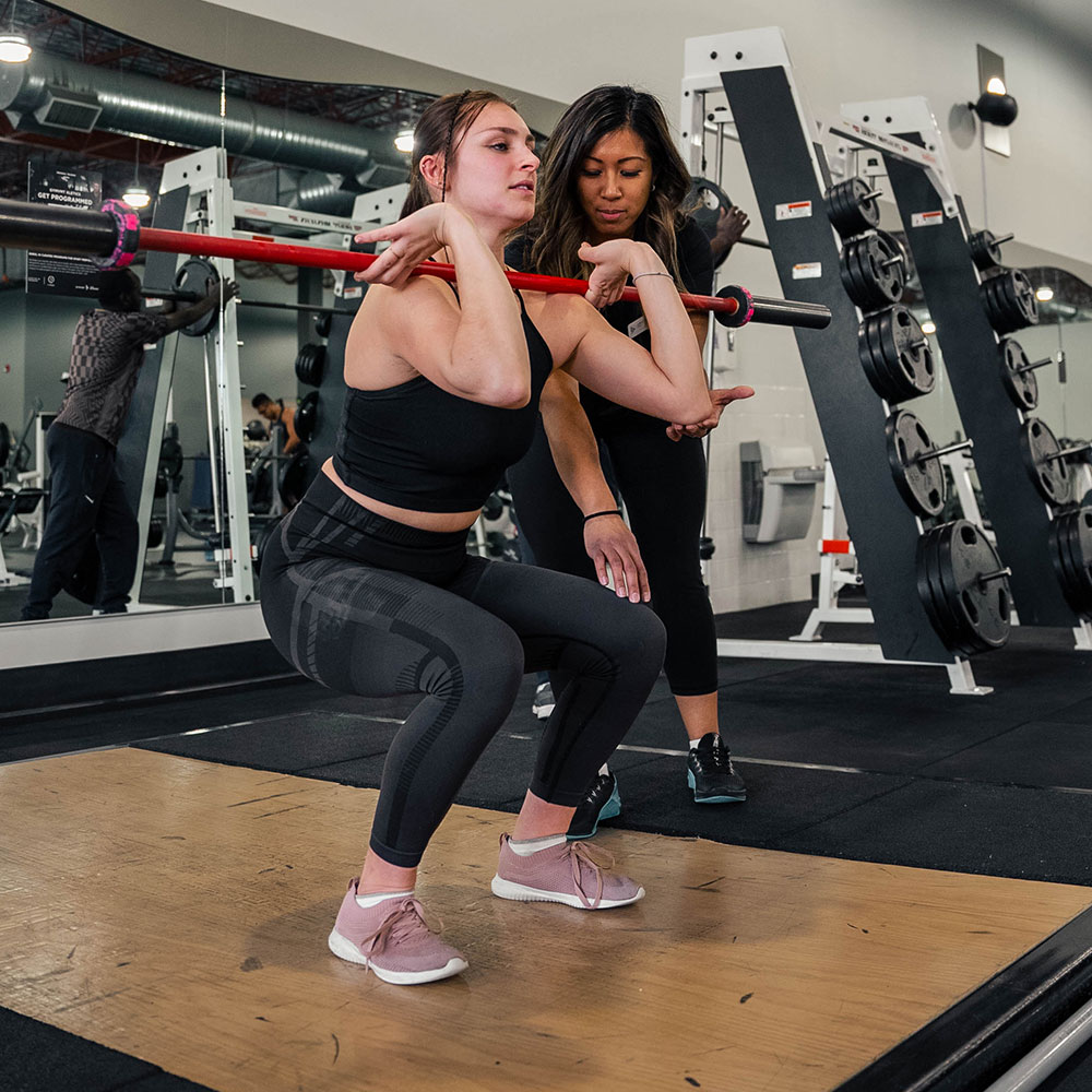 Woman front squatting with a personal trainer in Calgary